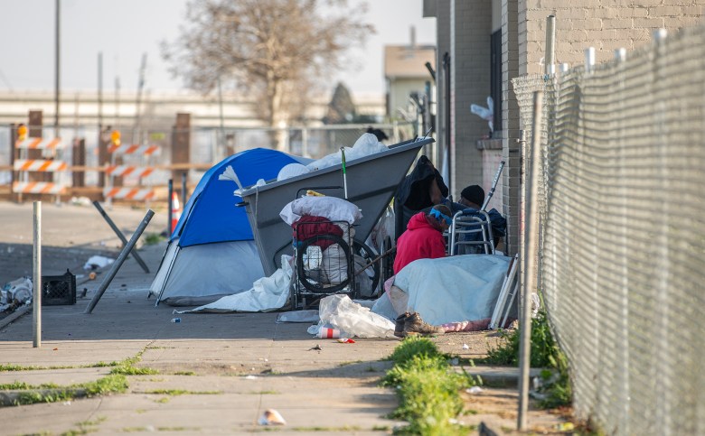 People sit on the sidewalk of G Street in a small homeless encampment in the Chinatown neighborhood of Fresno on Feb. 10, 2022. Photo by Larry Valenzuela, CalMatters