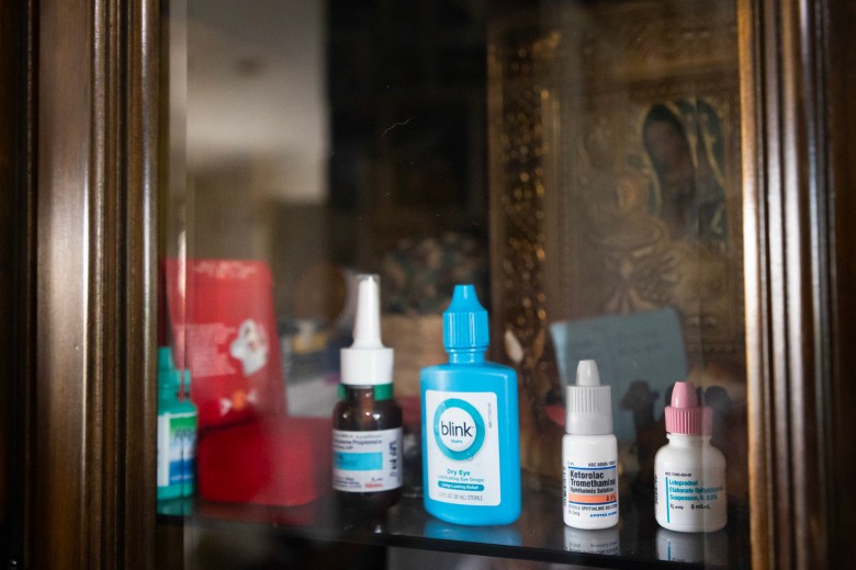 A blue eyedrop container and various other medicine containers on a shelf at a home.