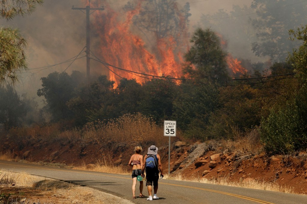 People walk on the road near flames and smoke plumes rising as firefighters continue to tackle the Park Fire near the northern Sacramento Valley city of Chico on July 25, 2024. Photo by Fred Greaves, REUTERS