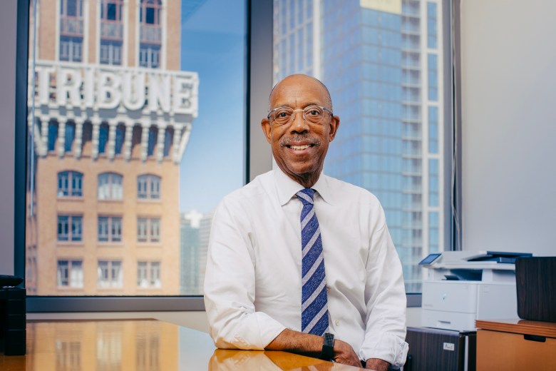 University of California President Michael V. Drake sits at a desk in an office building while wearing a button-up shirt and tie.