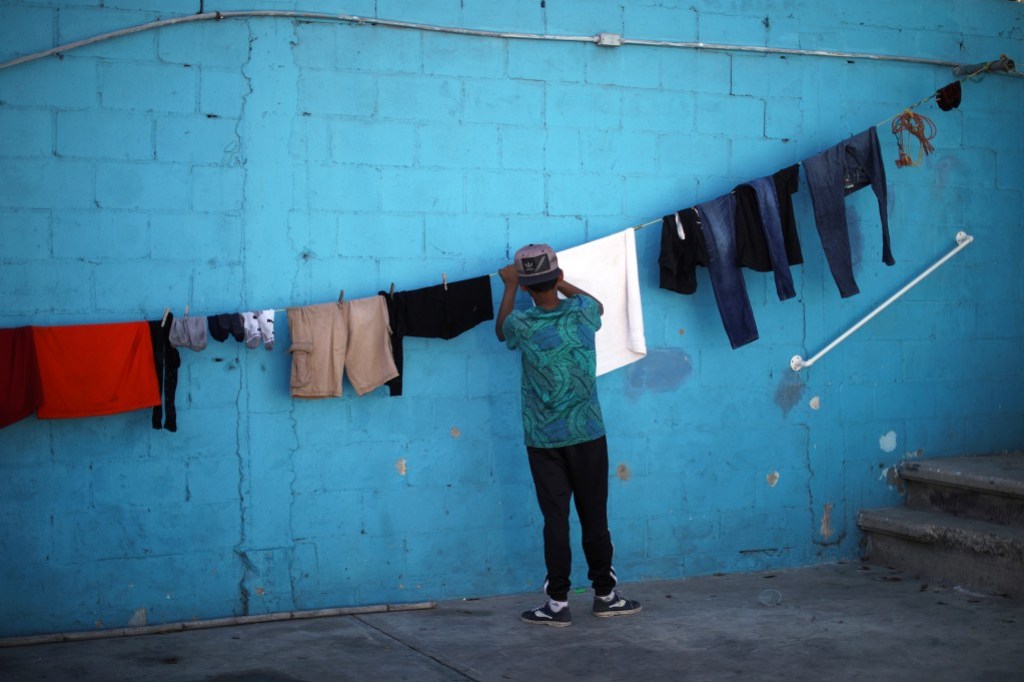 A young boy hangs clothes to dry on a clothesline in front of a bright, light blue wall.